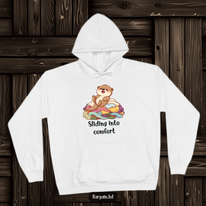 Funny hoodie featuring a cute otter gleefully sliding down a large pile of colorful garments, perfect for staying warm and cheerful.